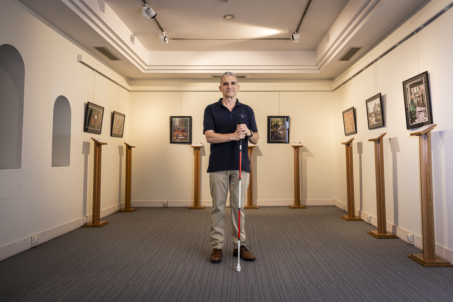 Rafael Zapata, con su bastón rojo y blanco que le identifica como persona con sordoceguera, rodeado de las fotos que expone en el Museo Tiflológico